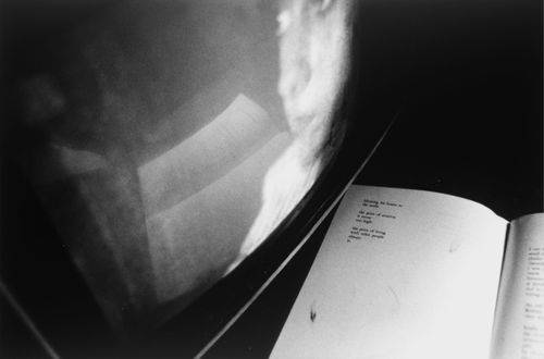 Bogside med digt spejles i tv-skærm, hvor der også ses et kvindeansigt.