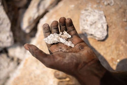 Nærbillede af en hånd, der holder lyse stenstykker med lithiumholdigt materiale i en mine. Billedet illustrerer udvinding af lithium, som er et vigtigt råstof i batterier og den grønne omstilling.