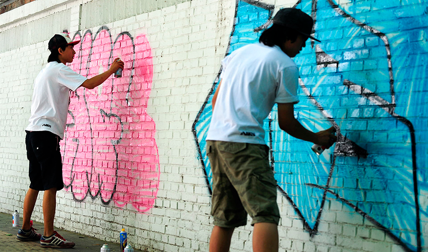 Graffitimalere spraymaler tags på en hvid mur.